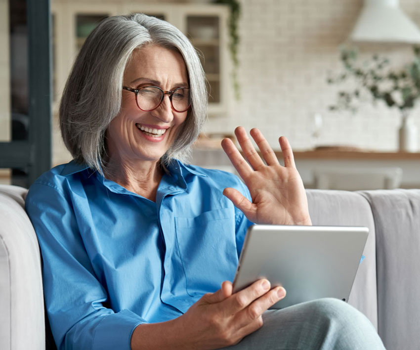 Happy 60s older mature middle aged adult woman waving hand holding digital tablet